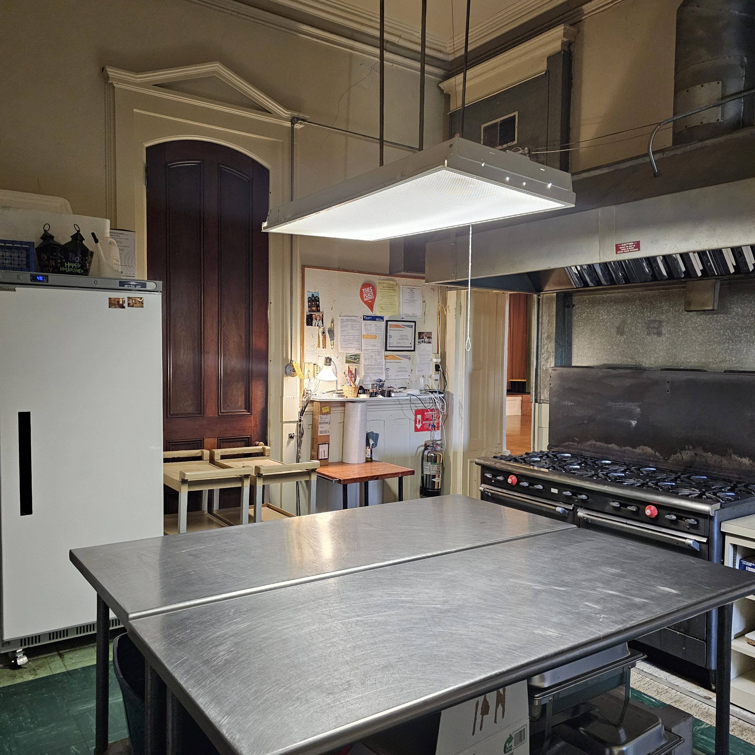 An industrial kitchen with a prep table, stove, and fridge