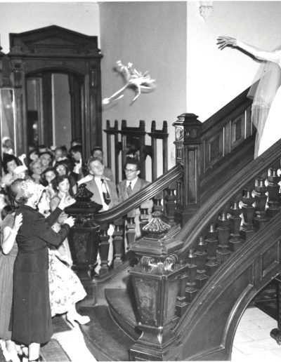 A black and white photo of a bride (circa 1940s) tossing her bouquet down the stairs